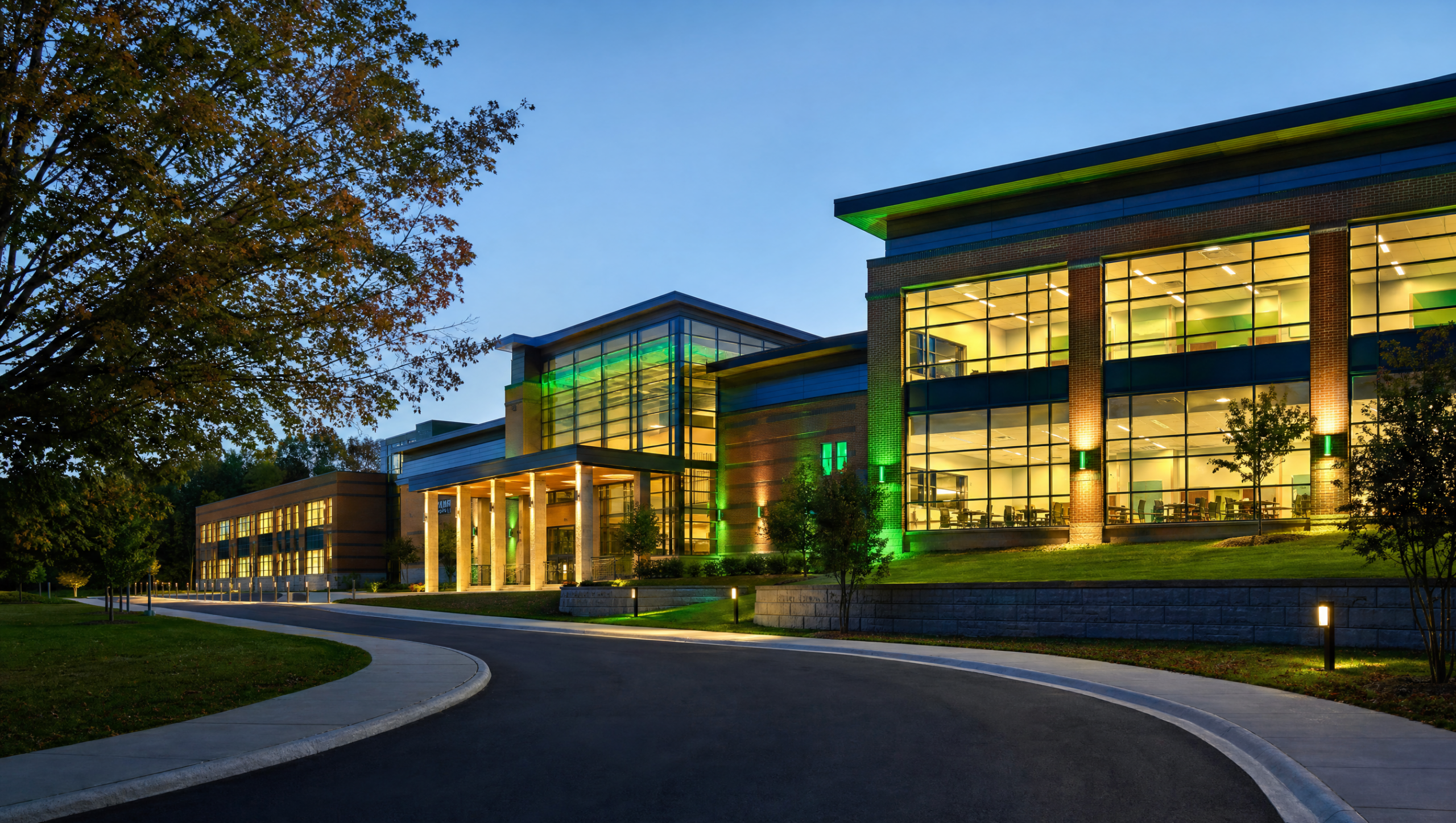 Modern school campus building exterior at dusk with warm interior classroom lighting glowing through large windows